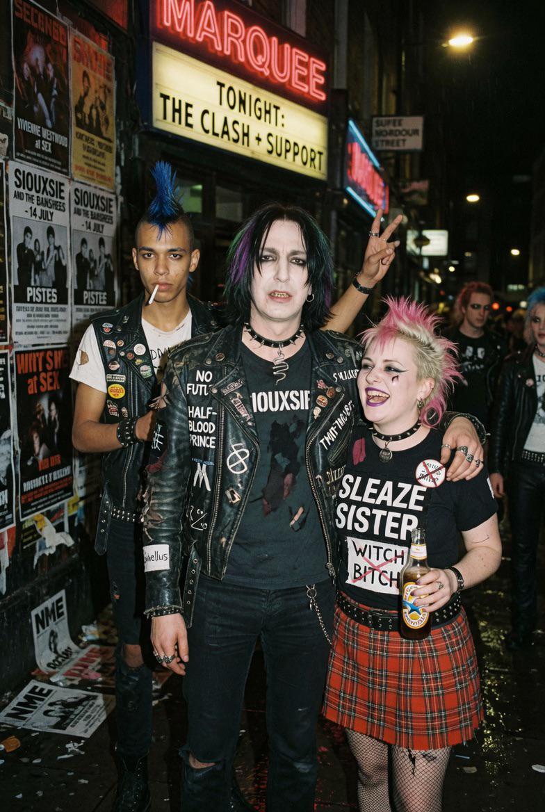 Three individuals in a gritty urban street scene outside a music venue, showcasing unique punk fashion.