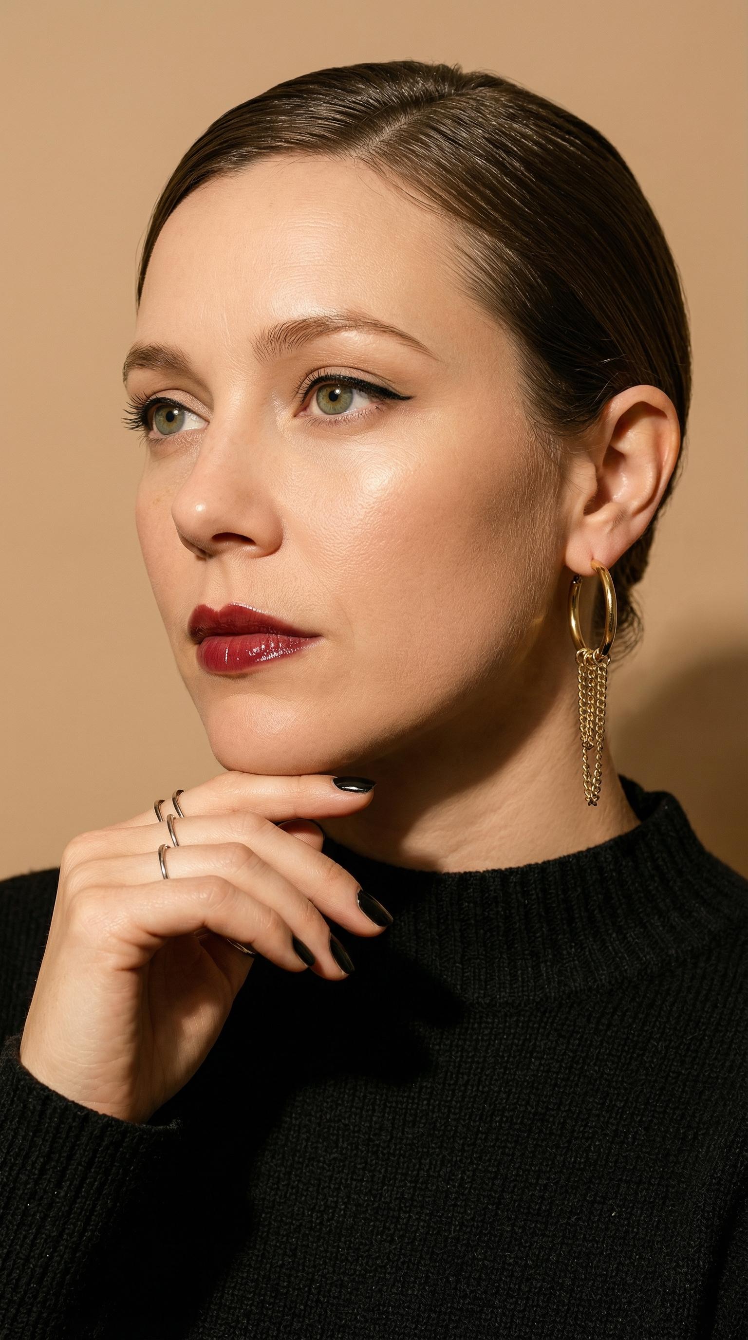 Close-up portrait of an elegant woman with slicked-back hair and glossy burgundy lips, thoughtful gaze directed off-camera.