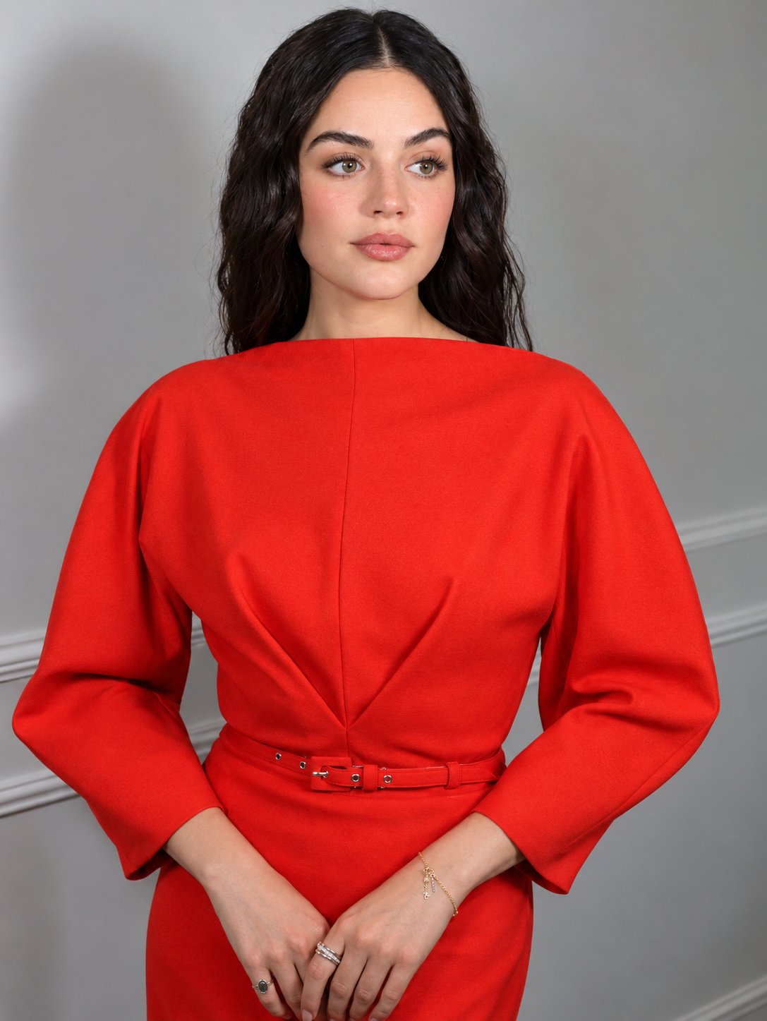Elegant woman in bright red long-sleeve fitted dress standing confidently in a studio with soft diffused lighting.