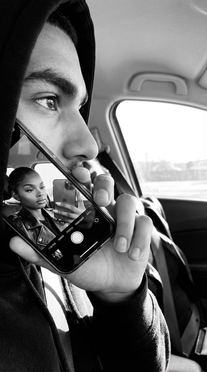Close-up of a person in a car holding a phone in a mirror-like reflection.