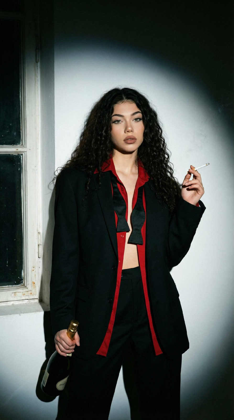 A cinematic close-up portrait of a woman in an oversized suit, holding champagne and a cigarette against a dark studio backdrop.