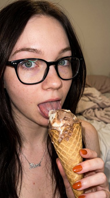 Close up of a woman licking chocolate ice cream in a waffle cone, framed by soft indoor lighting.