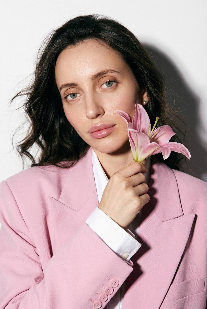Close-up macro portrait featuring a woman with a pink lily pressed to her cheek, showcasing vibrant skin texture and soft lighting.