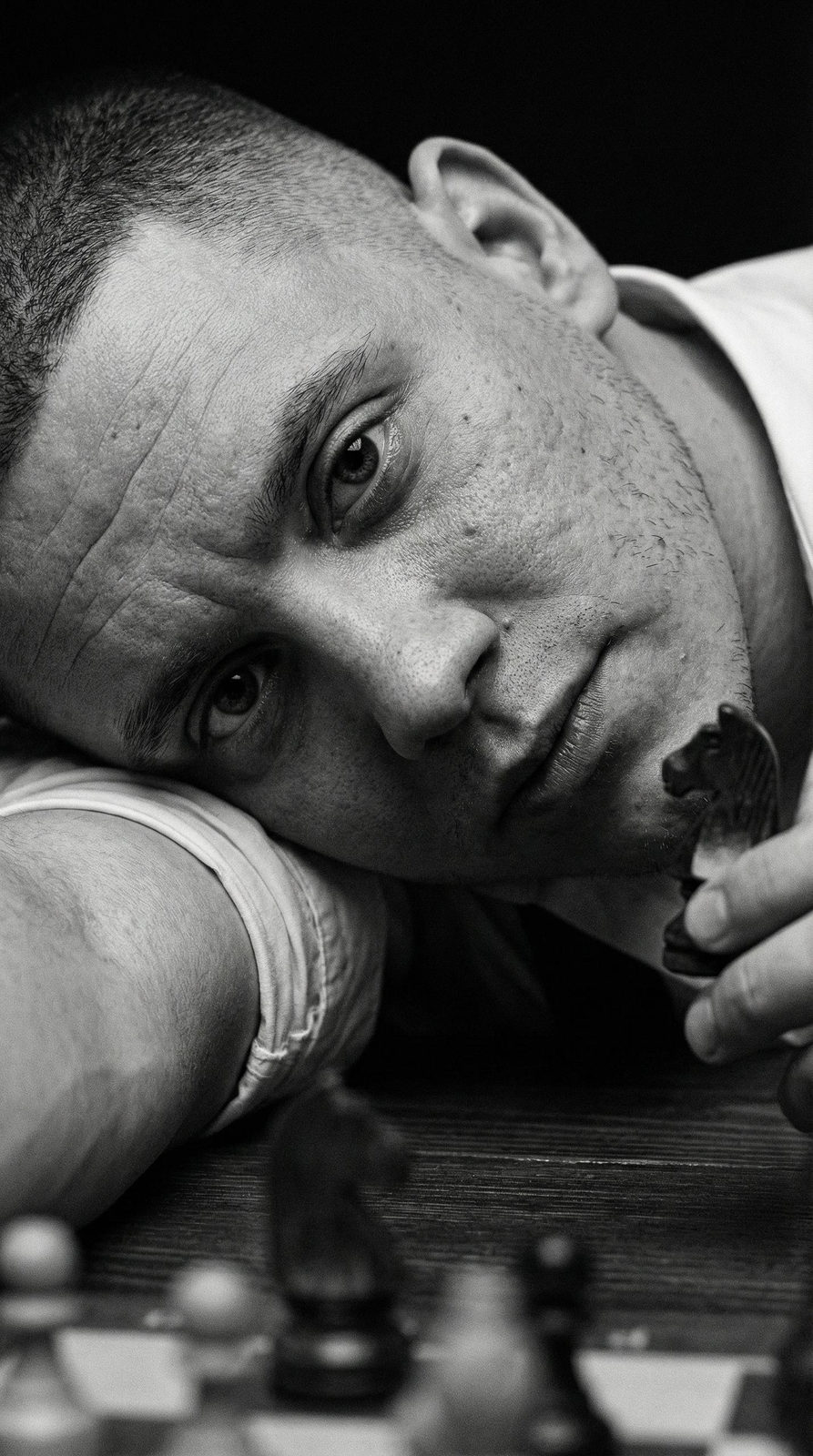 Ultra-detailed extreme close-up portrait of a man with intense eyes and visible skin textures, lying on a dark table.