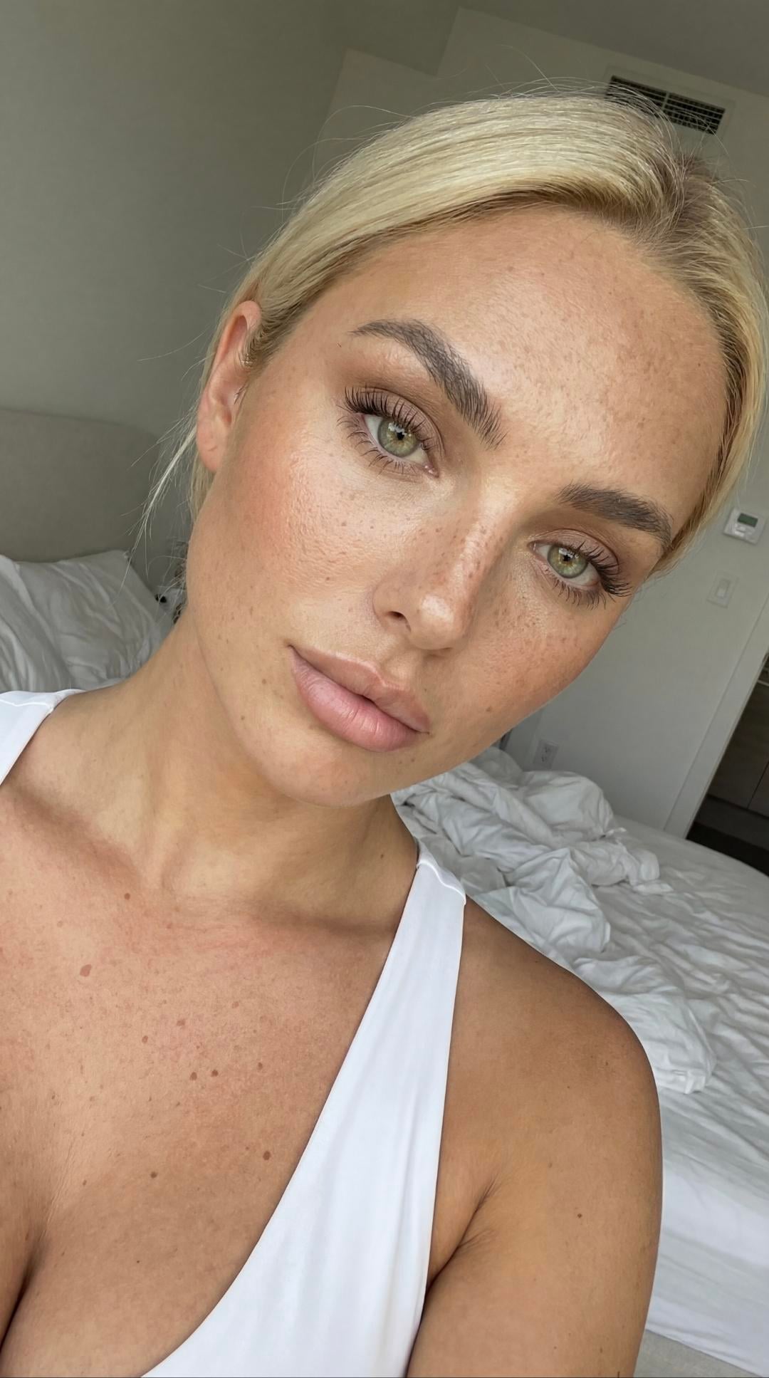 Close-up shot of a woman with a clear complexion and freckles, gazing directly at the camera, hair loosely pulled back, soft natural light.