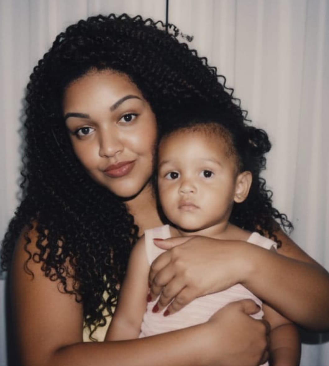 A soft-focus Polaroid-style photo of an adult and a child exchanging a warm embrace, bathed in gentle lighting with white curtains in the background.