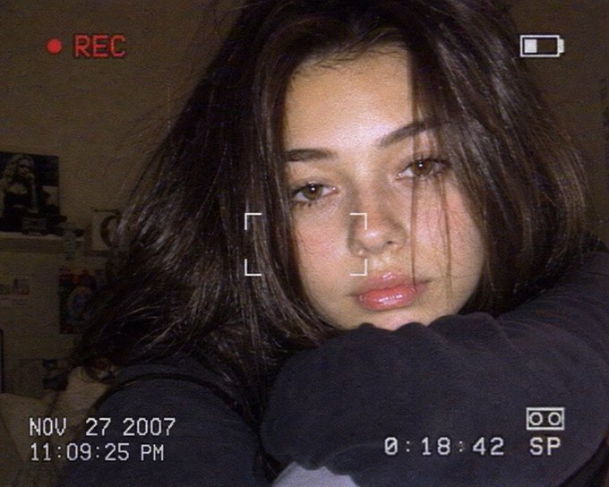 Close-up of a woman with dark voluminous hair resting her chin, warm lighting enhances her features in a cozy indoor setting.