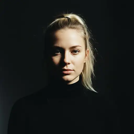 A young blonde woman with a ponytail in a black turtleneck, looking directly ahead in soft light with high contrast.