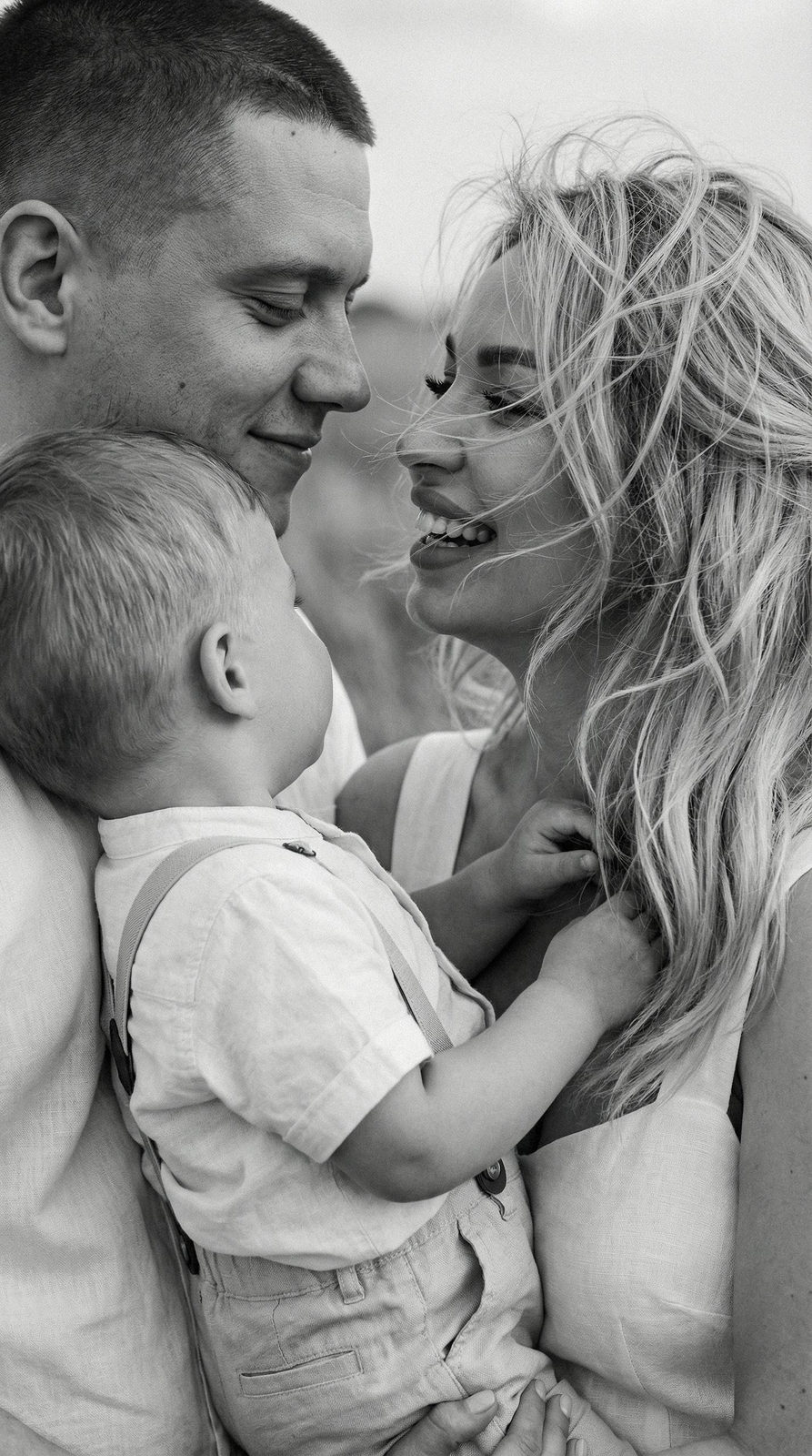 Close-up of a family of three smiling softly against a blurred field background, capturing intimate emotions.