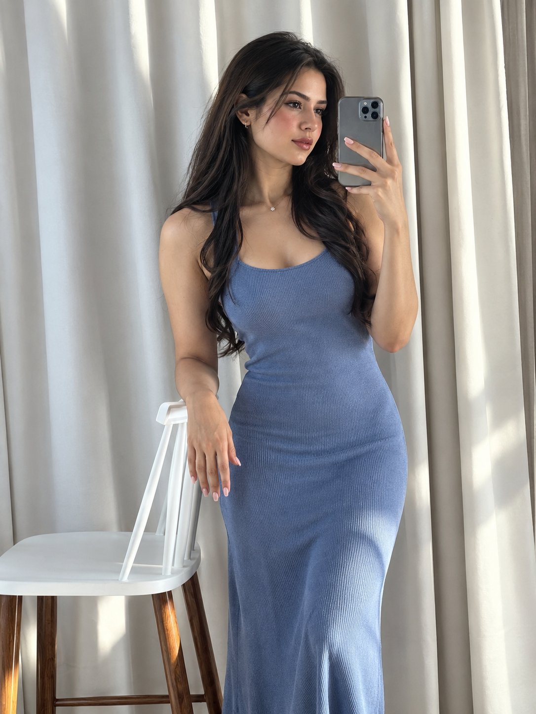 Ultra-realistic mirror selfie of a woman in a fitted ribbed powder blue sleeveless midi dress, indoors by soft curtains.