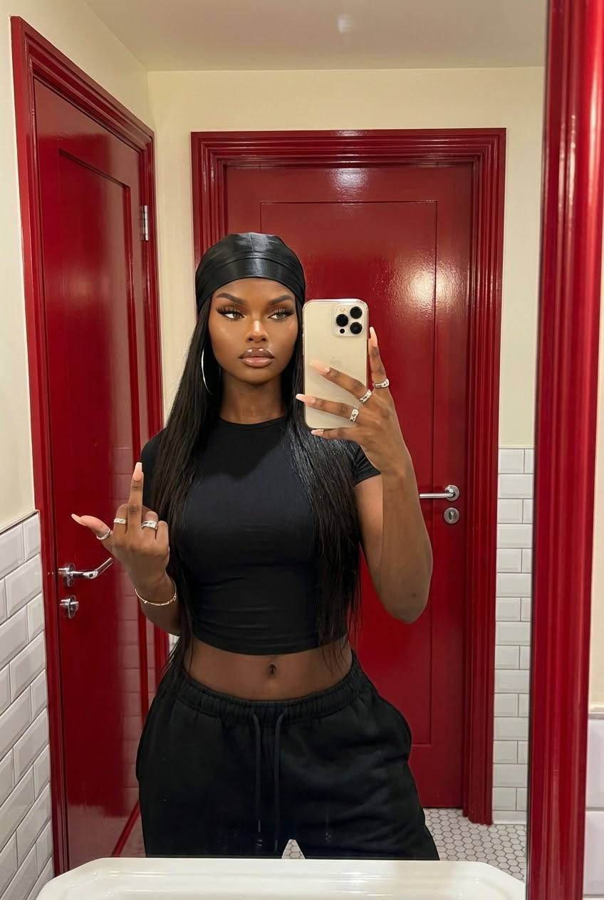 A confident young woman in a bathroom taking a mirror selfie, showcasing a stylish outfit and long hair.
