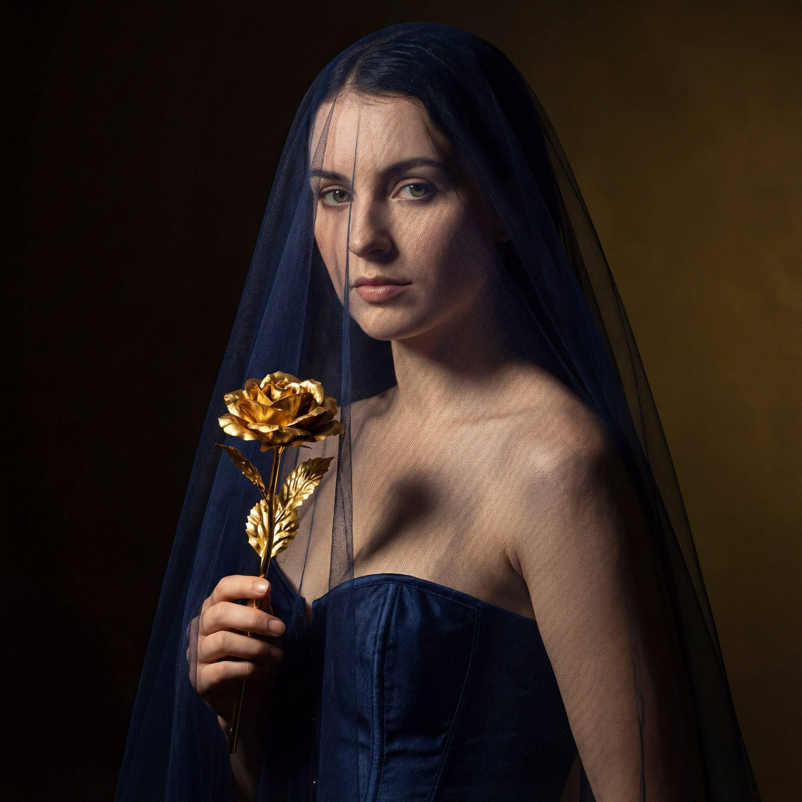A dramatic close-up portrait of a veiled woman holding a golden rose, illuminated by side lighting.
