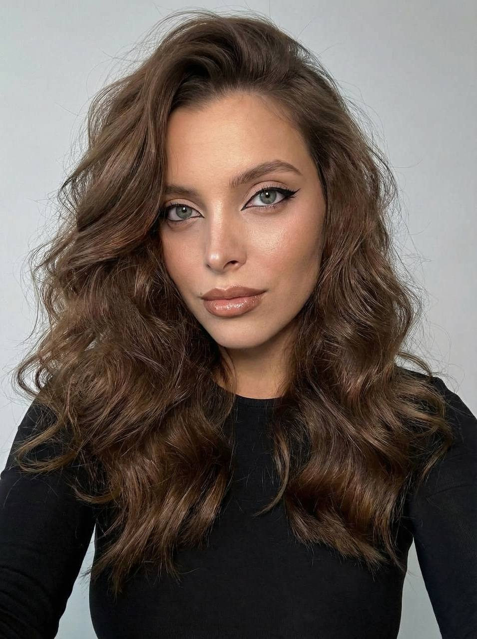 Close-up portrait of a girl with long, wavy hair and expressive eyes, wearing makeup.