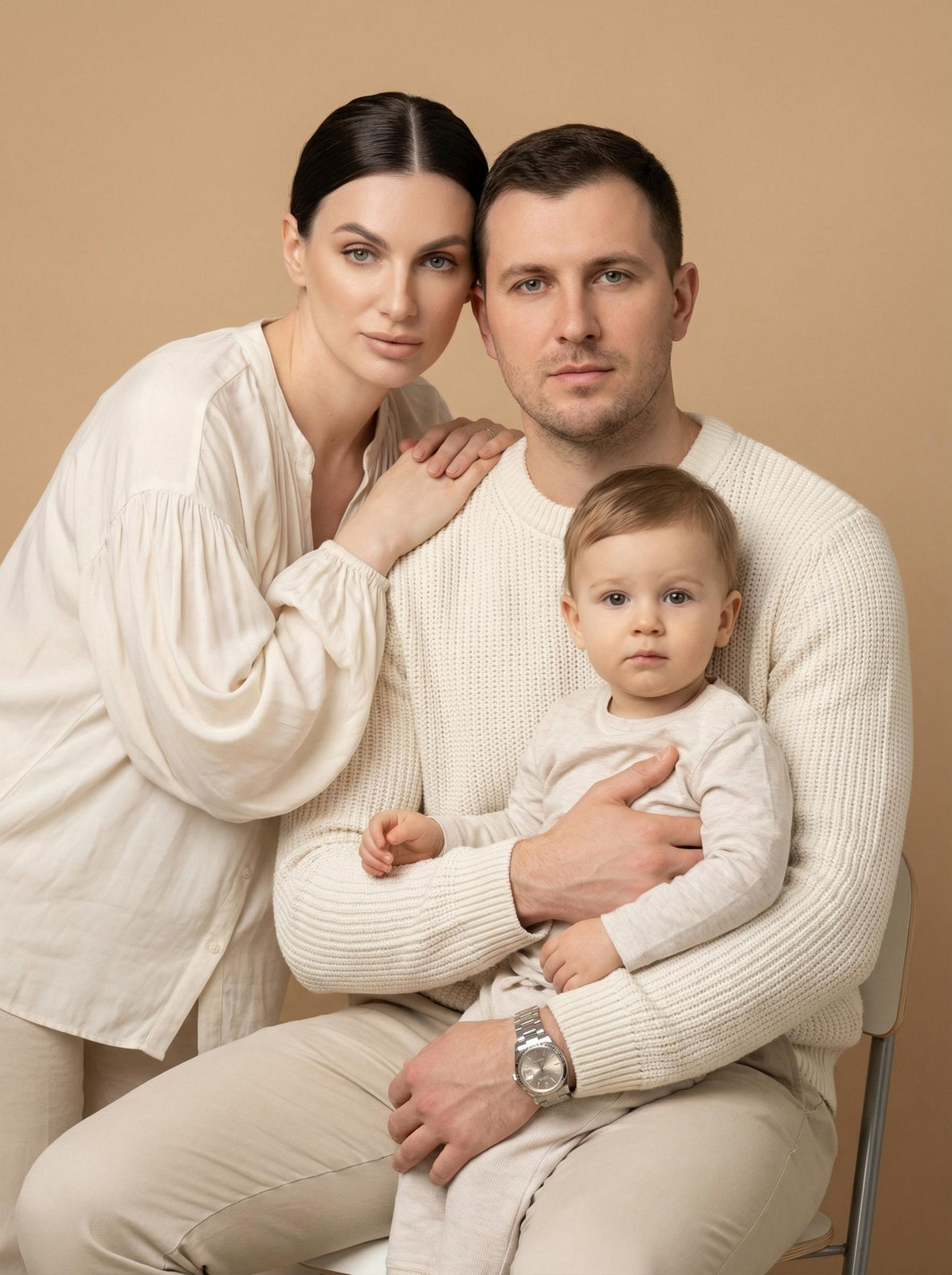 A family portrait featuring three individuals in a minimalist studio, with soft lighting and a warm beige background.