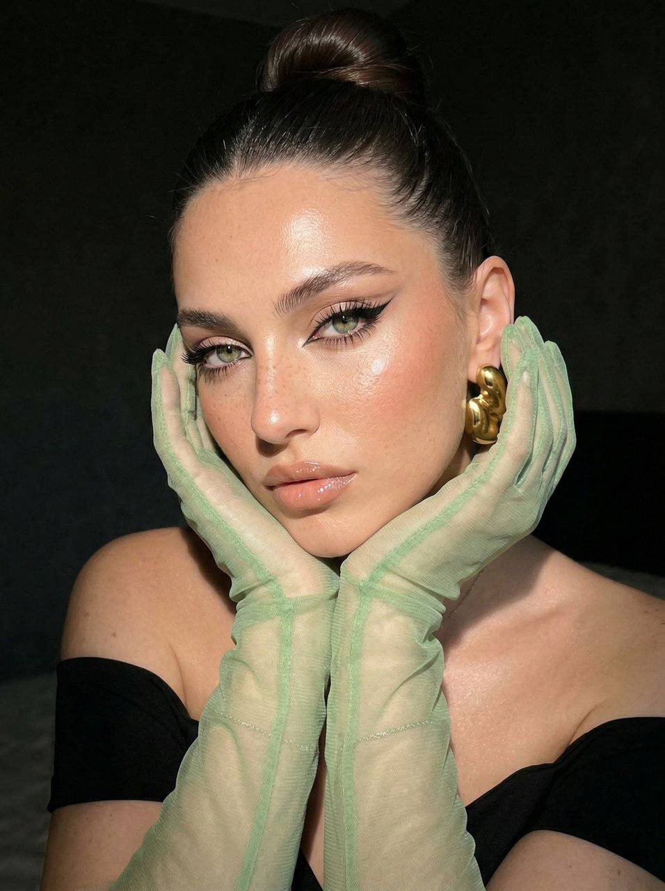 Close-up of a glamorous girl with vibrant makeup and an elegant hair bun, showcasing cat-eye eyeliner and polished skin.