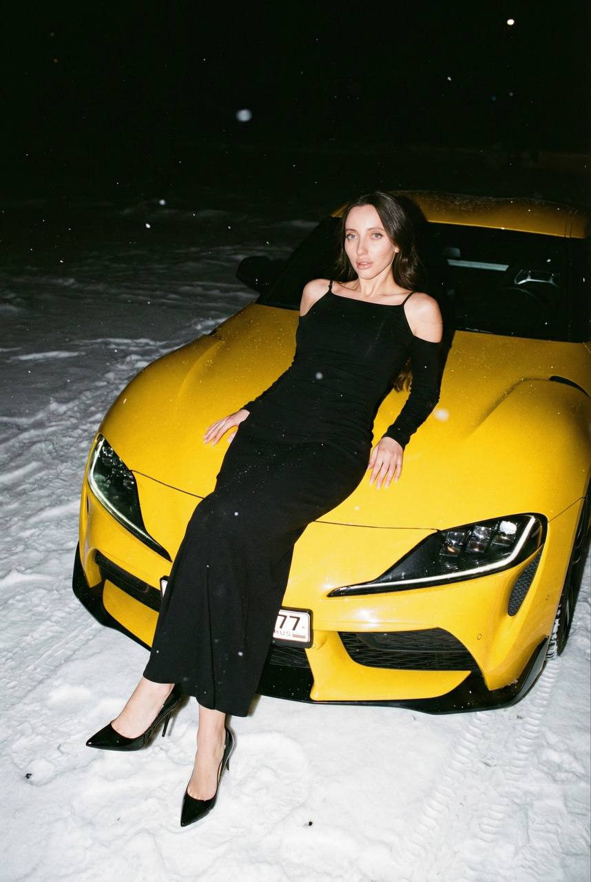Glamorous woman in a yellow sports car on snow, wearing an elegant long dress, captured in night film flash style.