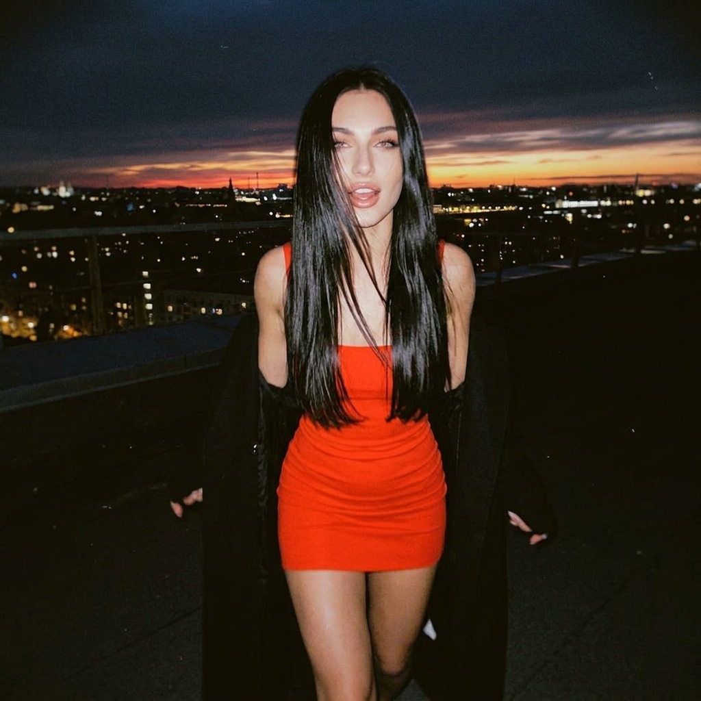A woman in a bright red dress running on a rooftop at night, with a black coat slipped off her shoulders and wind-blown hair.