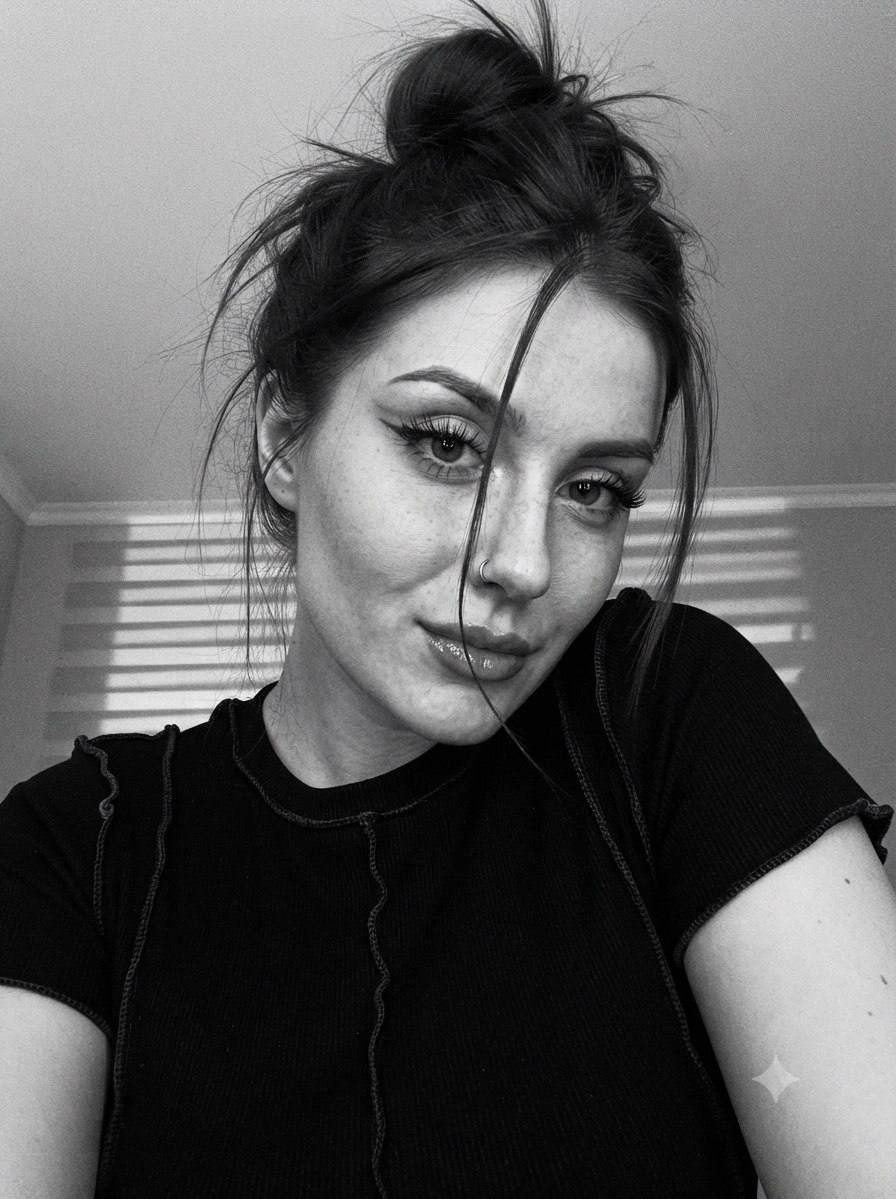 Close-up selfie with a high bun hairstyle and dim lighting. Shadows create depth on the face.