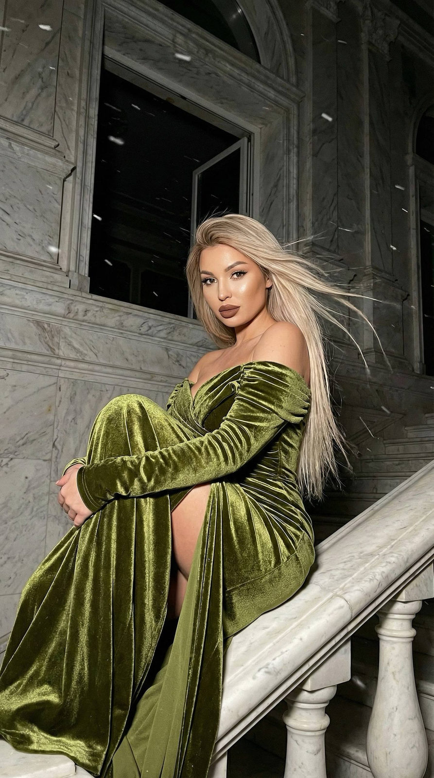 Close-up portrait of a woman in an olive velvet dress on a marble staircase, with flowing hair and snow gently falling.