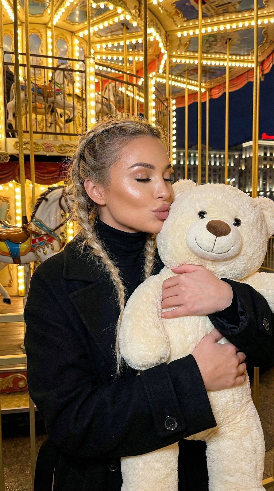 Dreamy portrait of a girl blowing a kiss with a plush bear against a brightly lit carousel background.