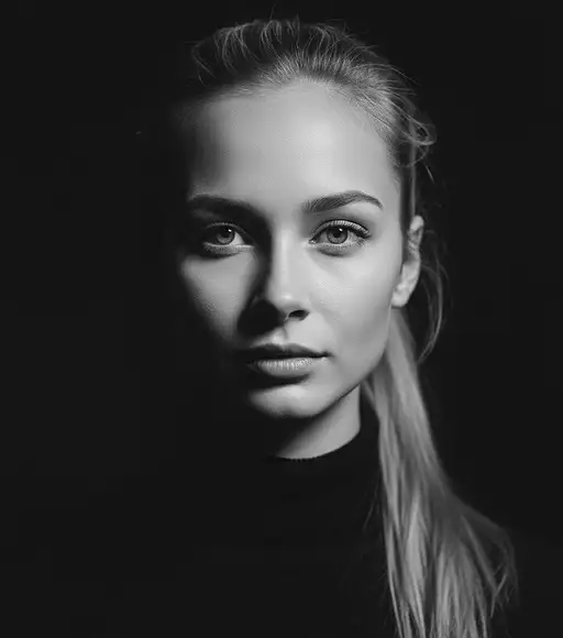 Headshot of a young blonde woman with a ponytail in a black turtleneck, captured in soft light.
