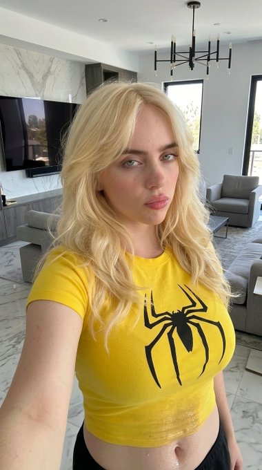 A medium close-up selfie of a person in a yellow crop top with a spider graphic, set in a bright living room.