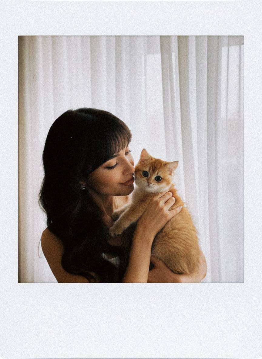 A warm Polaroid-style photo of a person holding a pet against soft curtains, illuminated by diffused natural light.