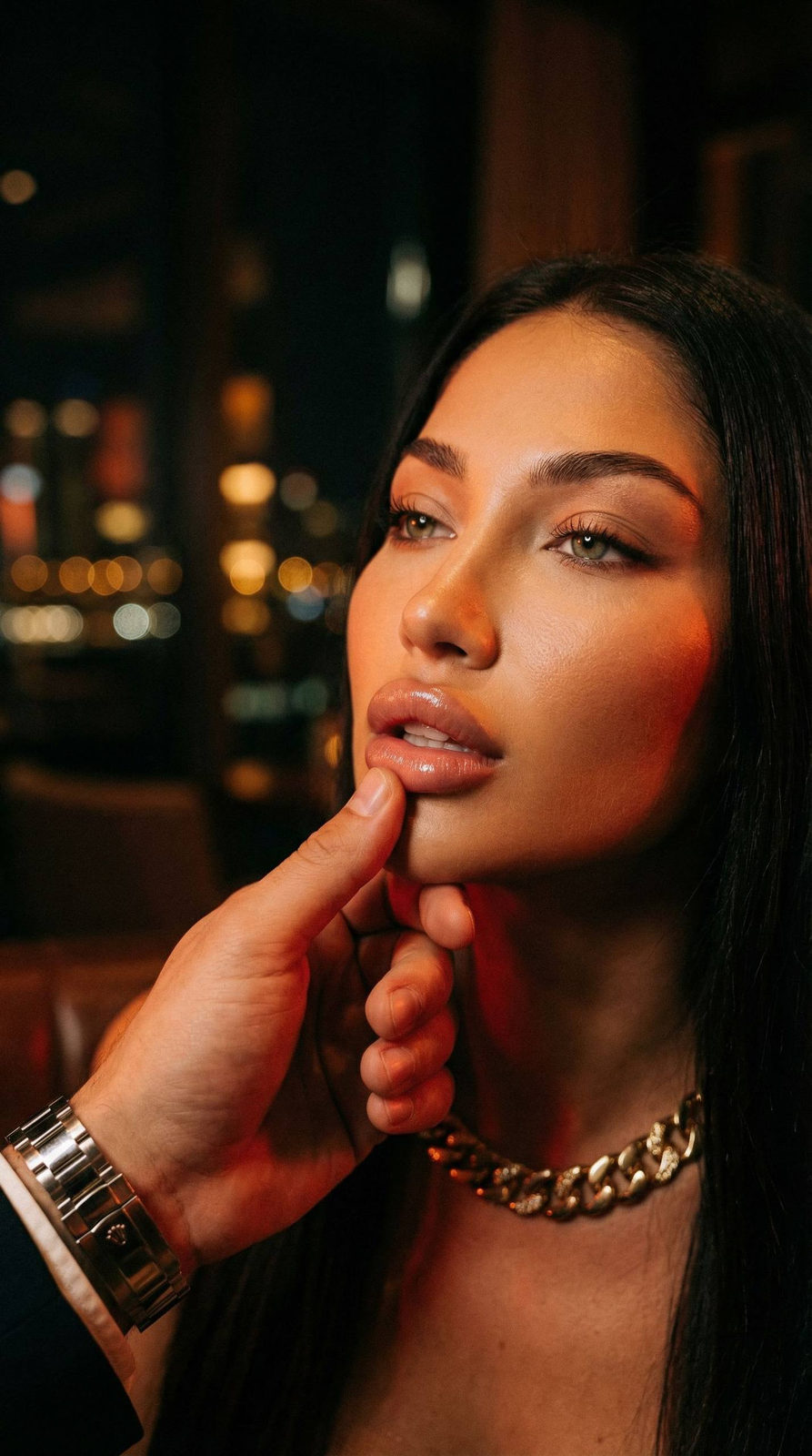A hyper-realistic night portrait of a woman in a dark lounge, her chin held gently by a man's hand.