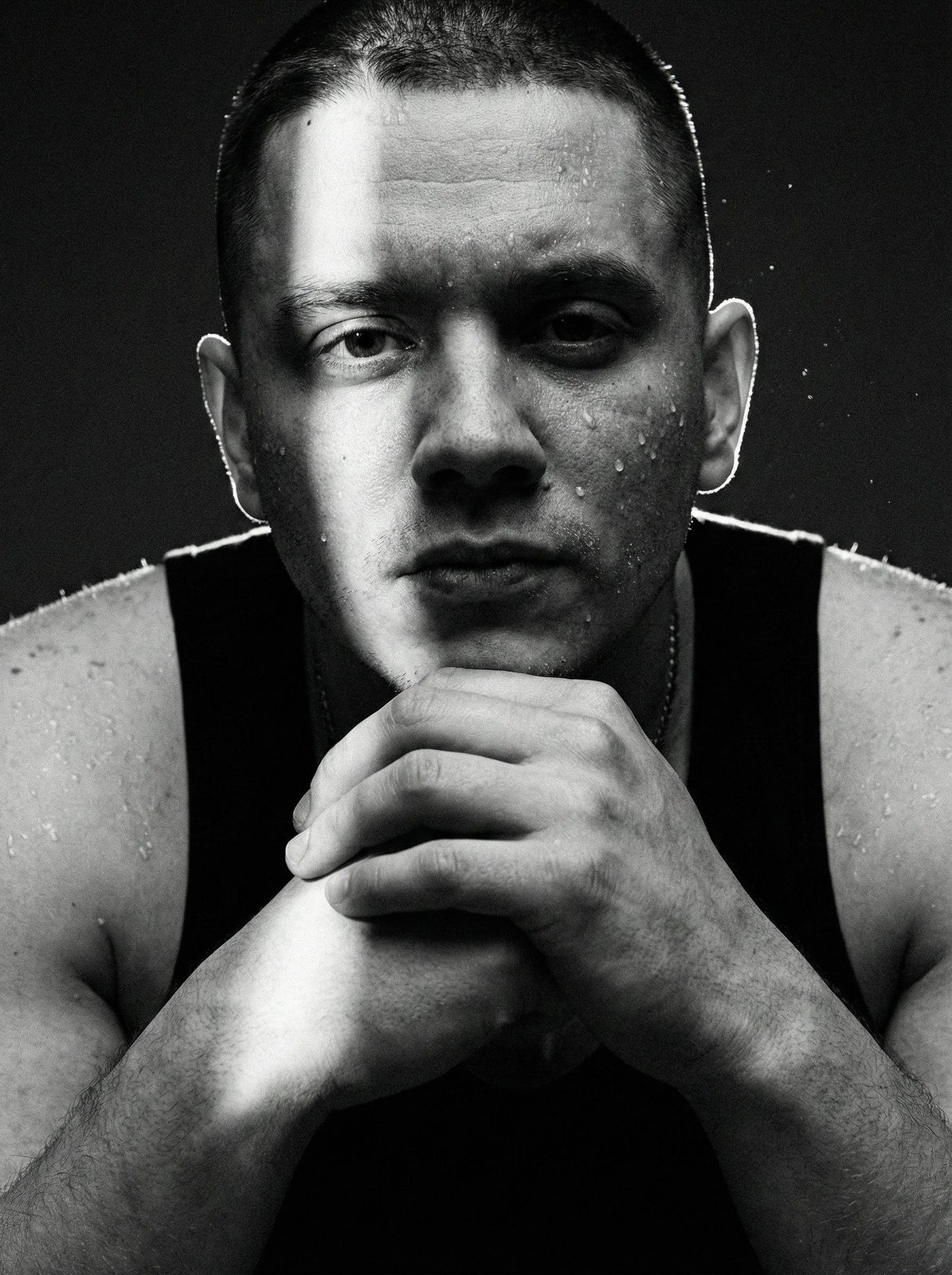 Extreme close-up of a muscular man in a tank top with splashes of water and dramatic lighting, capturing skin textures and contrasts.