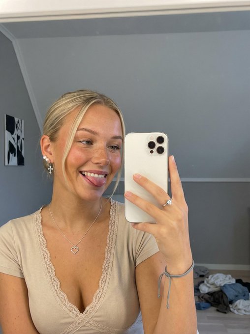 A joyful woman taking a mirror selfie with a playful smile, showcasing freckles and rosy blush.