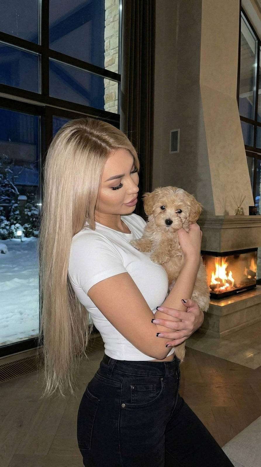 A girl in a cozy winter setting by a fireplace, holding a maltipoo puppy.