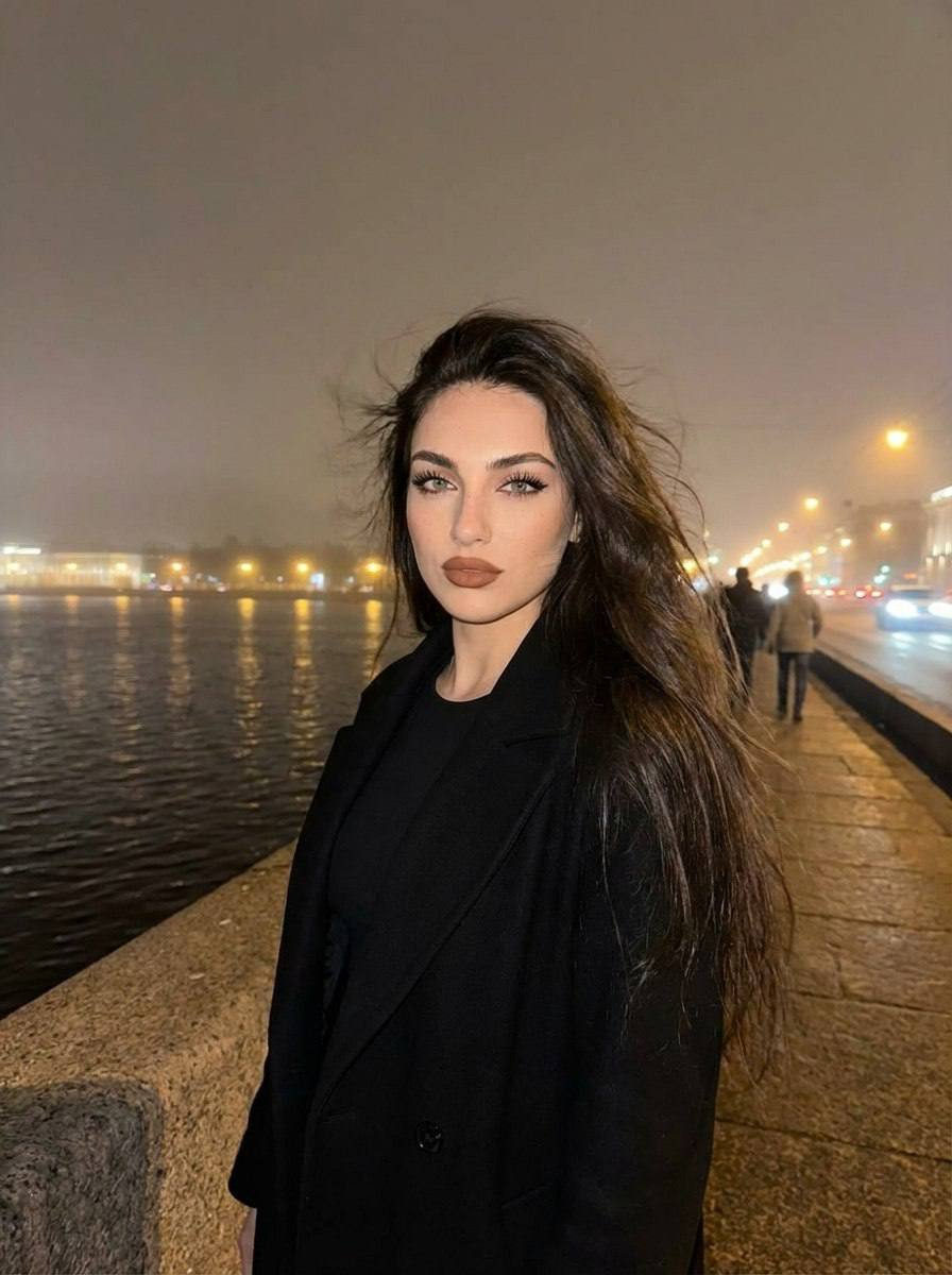 A girl in elegant clothes stands on a bridge over a river in St. Petersburg, illuminated by a flash, with long hair blowing in the wind.