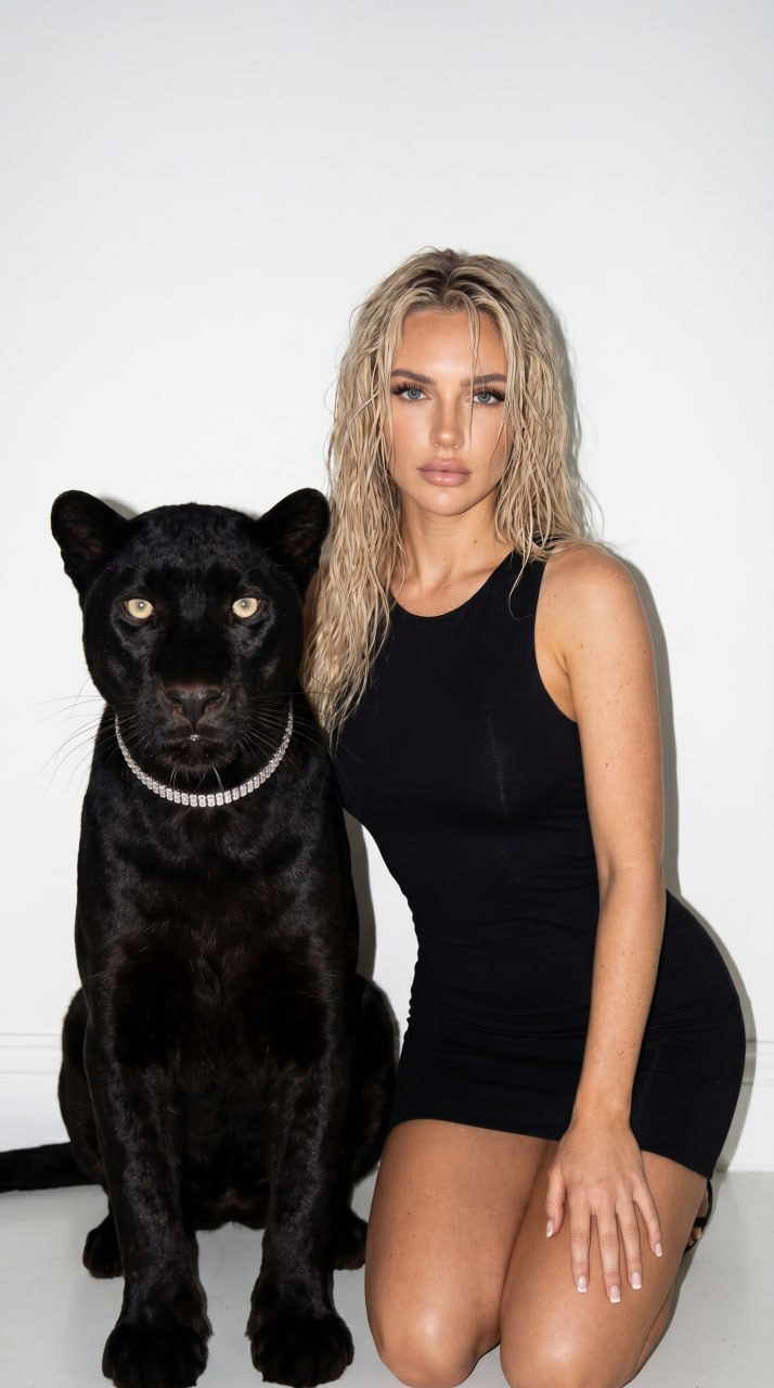 A woman in a fitted black dress kneeling beside a glossy black panther, both against a white wall.