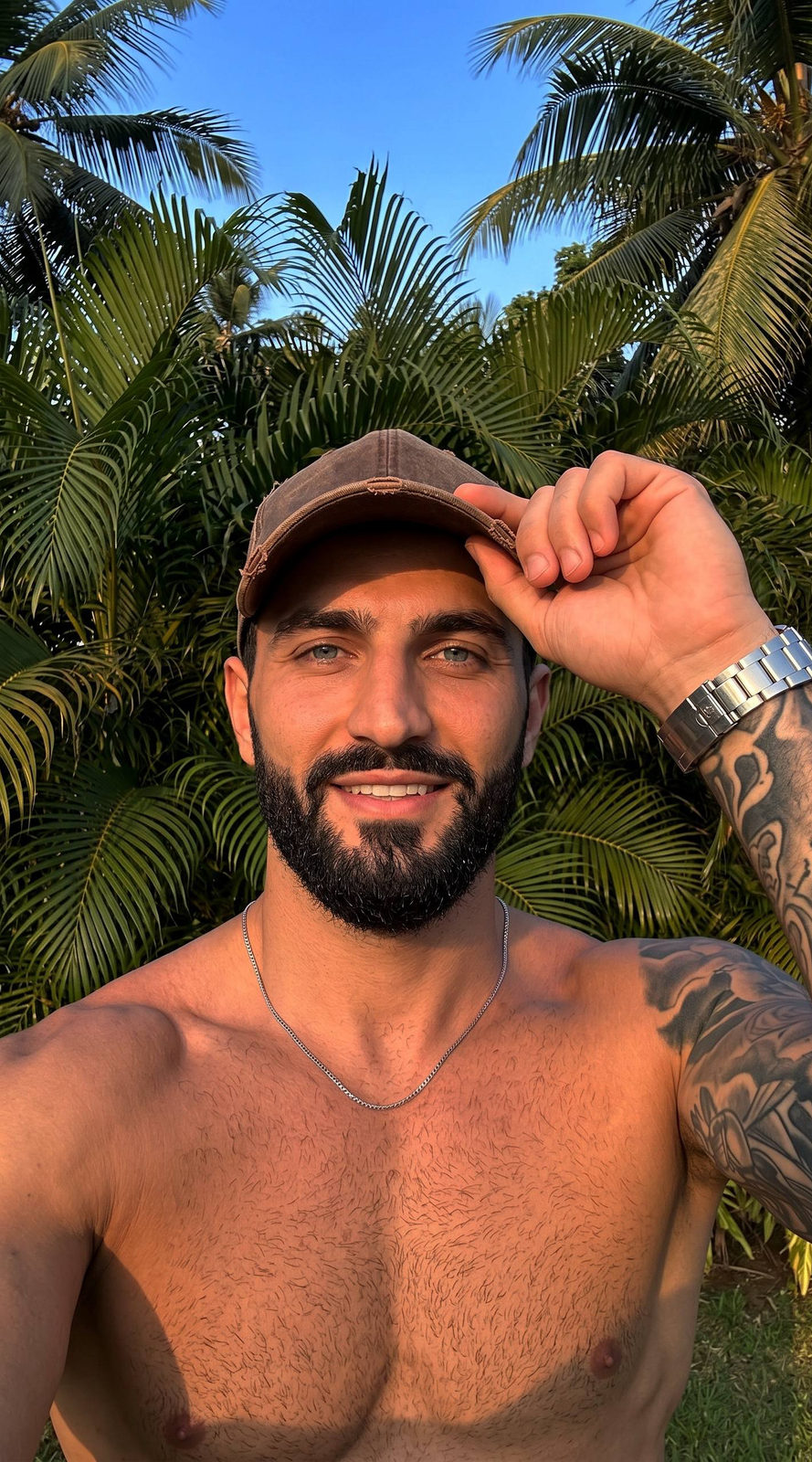 Close-up of man adjusting brown baseball cap with palm trees and sunset in background