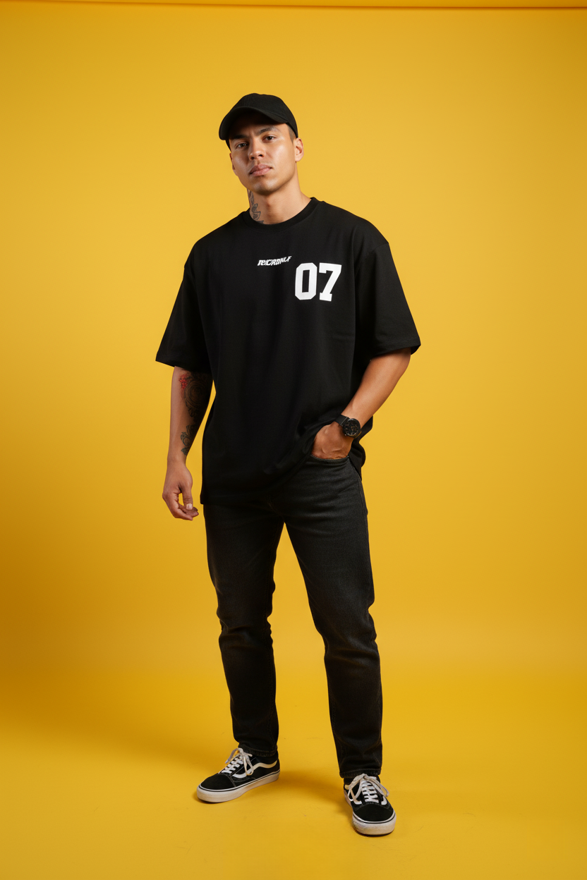 Confident Indonesian male model in oversized black tee against a vibrant yellow background, conveying modern street style.