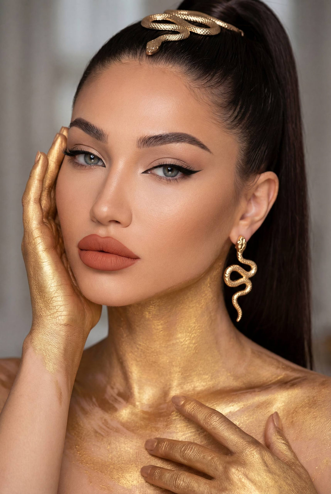 A woman with metallic gold paint on her neck and hands, featuring muted gray-blue eyes and a sleek high ponytail.