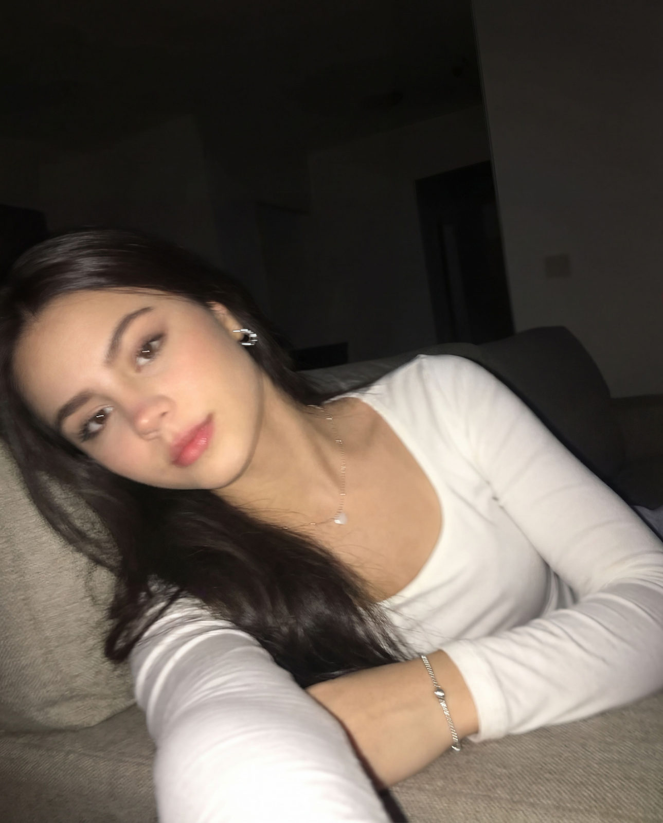 An iPhone selfie with subtle motion blur, showing uneven lighting and an awkward angle while sitting on a sofa at night.