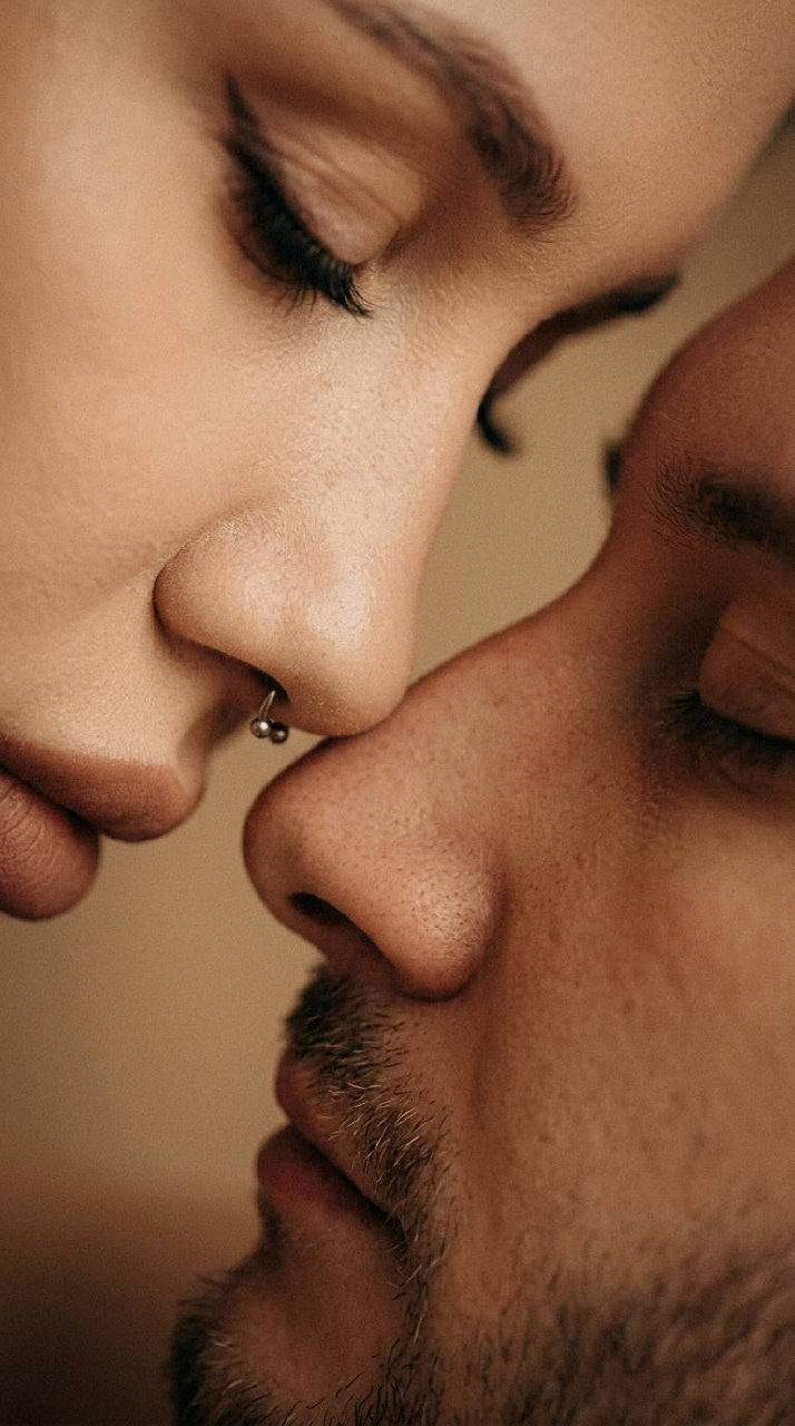 Extreme close-up of two noses touching, warm film grain, soft side lighting and beige tones.