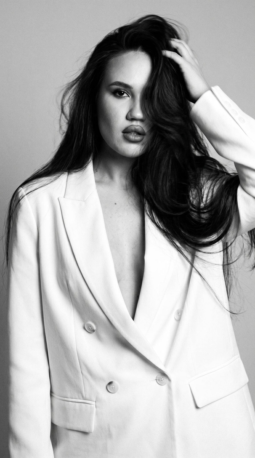 A stunning black and white portrait featuring a woman in an oversized white blazer, bold gaze, and voluminous hair.