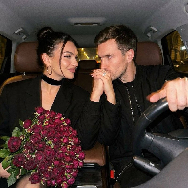 A warm, intimate scene of a couple inside a car, illuminated by soft dashboard lights and street lamps.