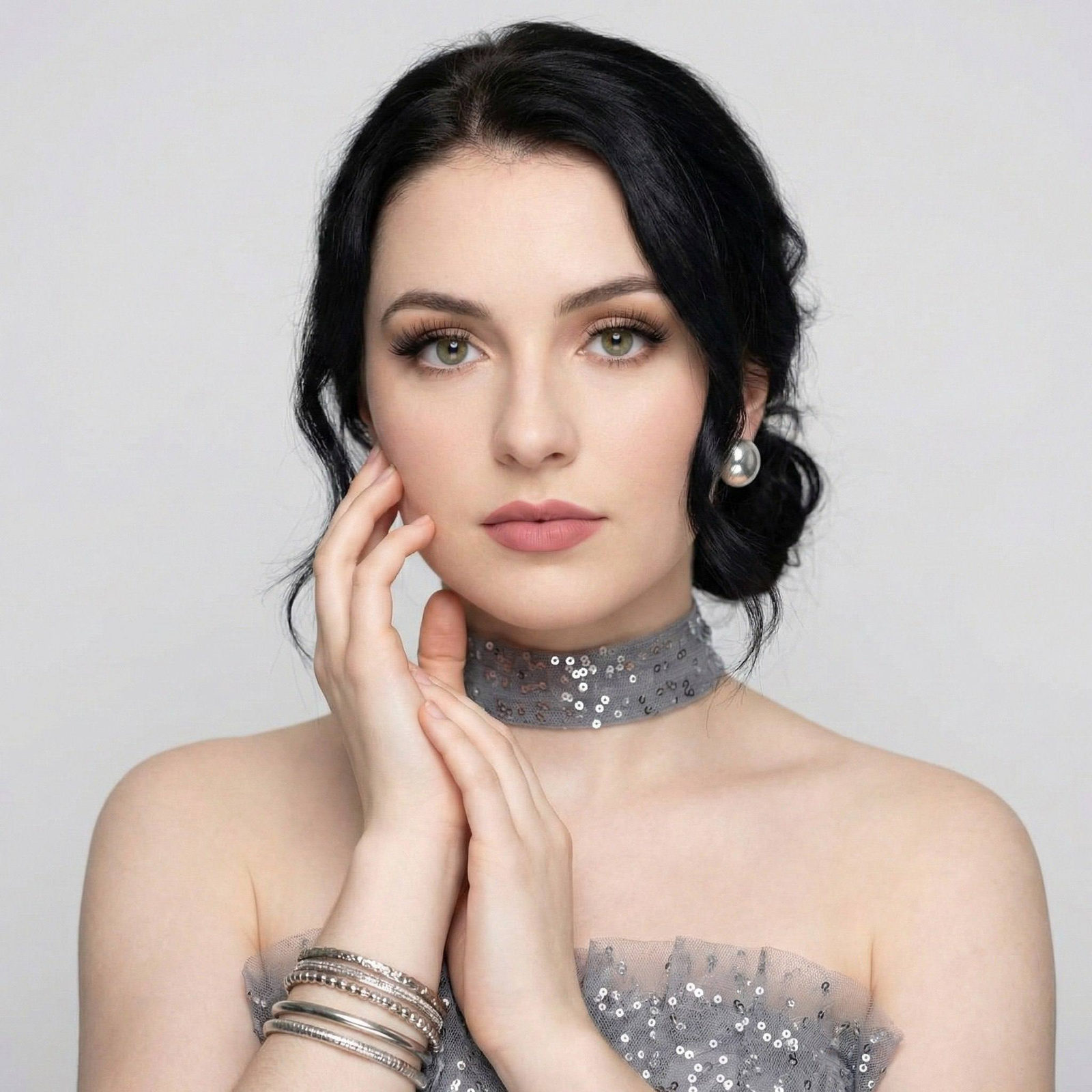 Close-up portrait of a woman in a textured gray tulle dress with shimmering silver sequins, softly lit in a light-gray studio.