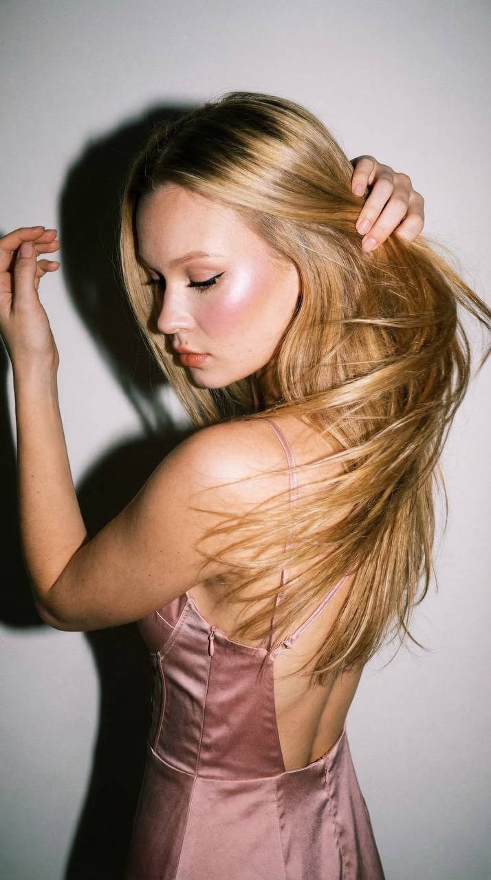 A woman in a dusty-pink dress with open back, captured in profile with harsh flash and dramatic shadows.