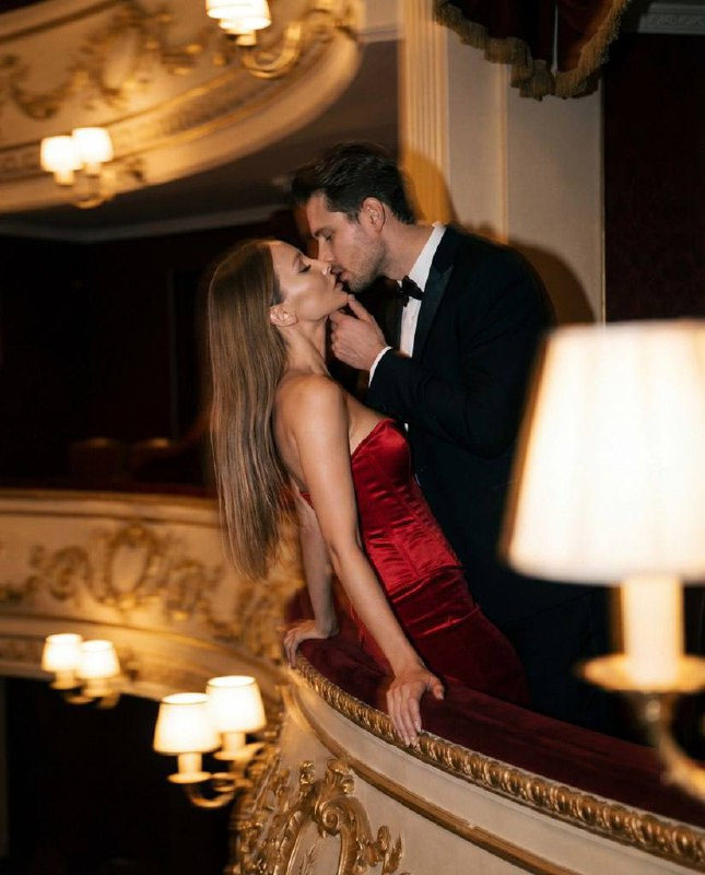 A romantic close-up of a couple kissing on a balcony, red velvet dress, dim lighting, with motion blur effect.