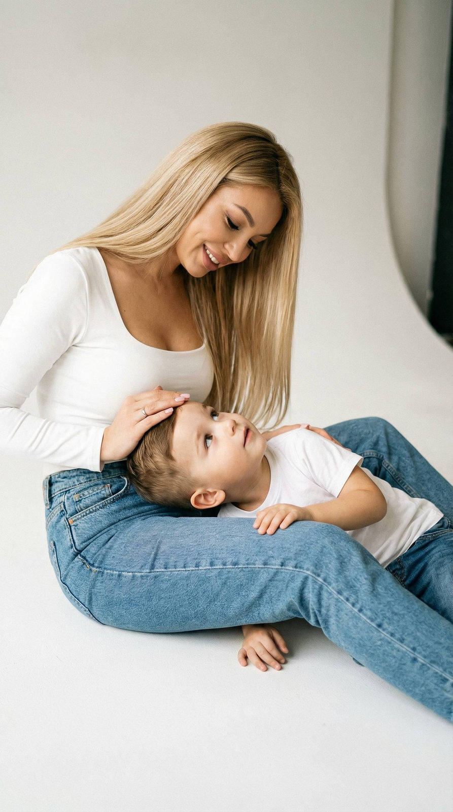 A warm portrait of a mother gently stroking her child's head while sitting on a cyclorama.