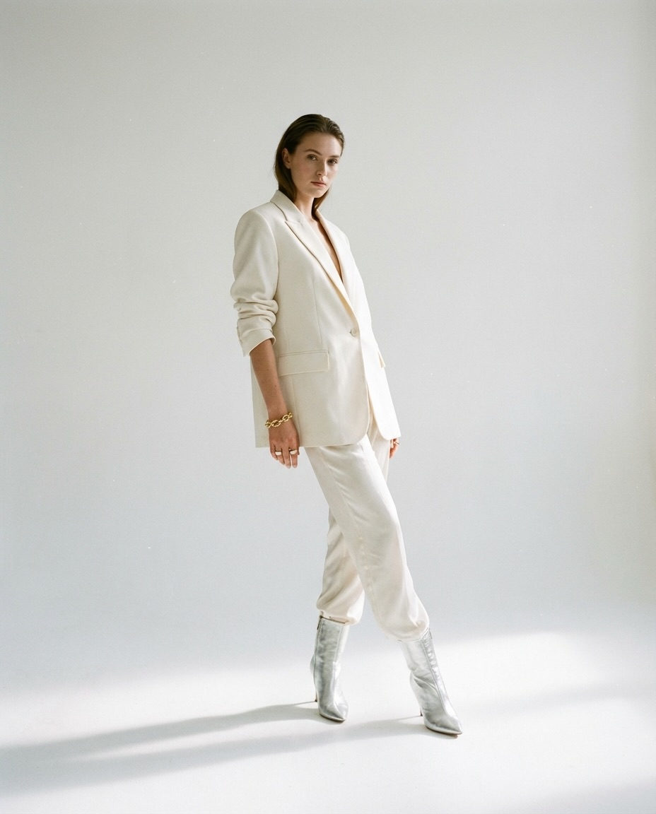 A full-body fashion portrait of a model in a pristine white cyclorama, captured in an elegant contrapposto pose with soft key lighting.