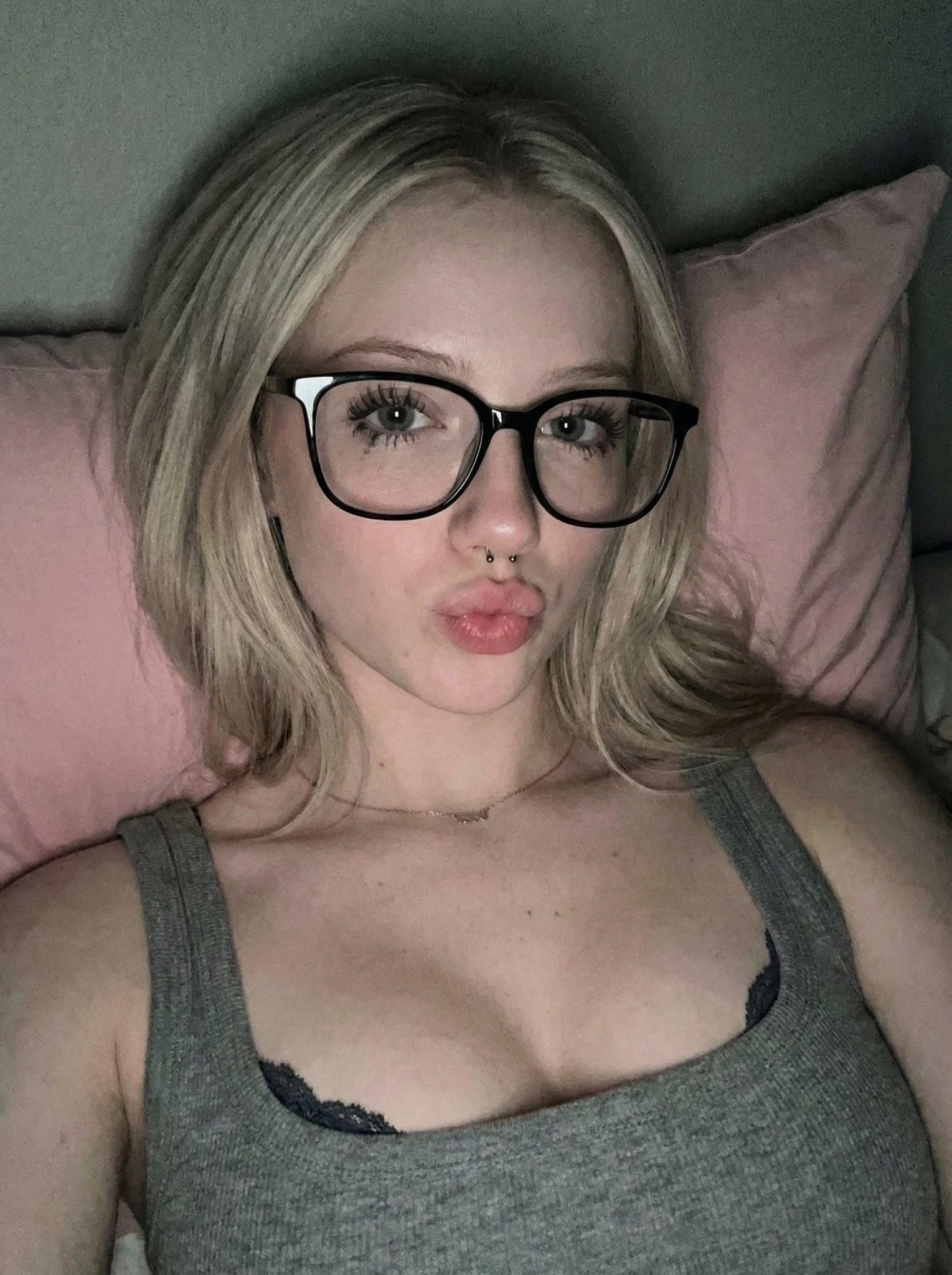 Close-up high-angle shot of a person on a pink pillow, styled hair and black-rimmed glasses.