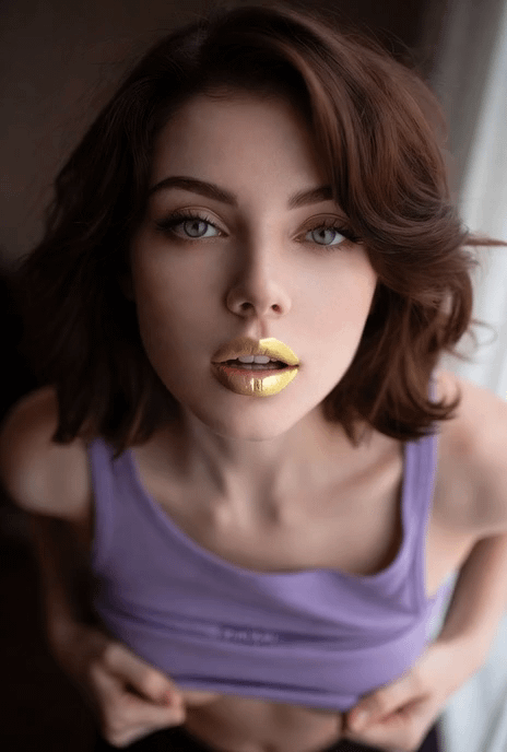 Model wearing a lavender tank top with gold lipstick, posed against a softly blurred concrete wall.