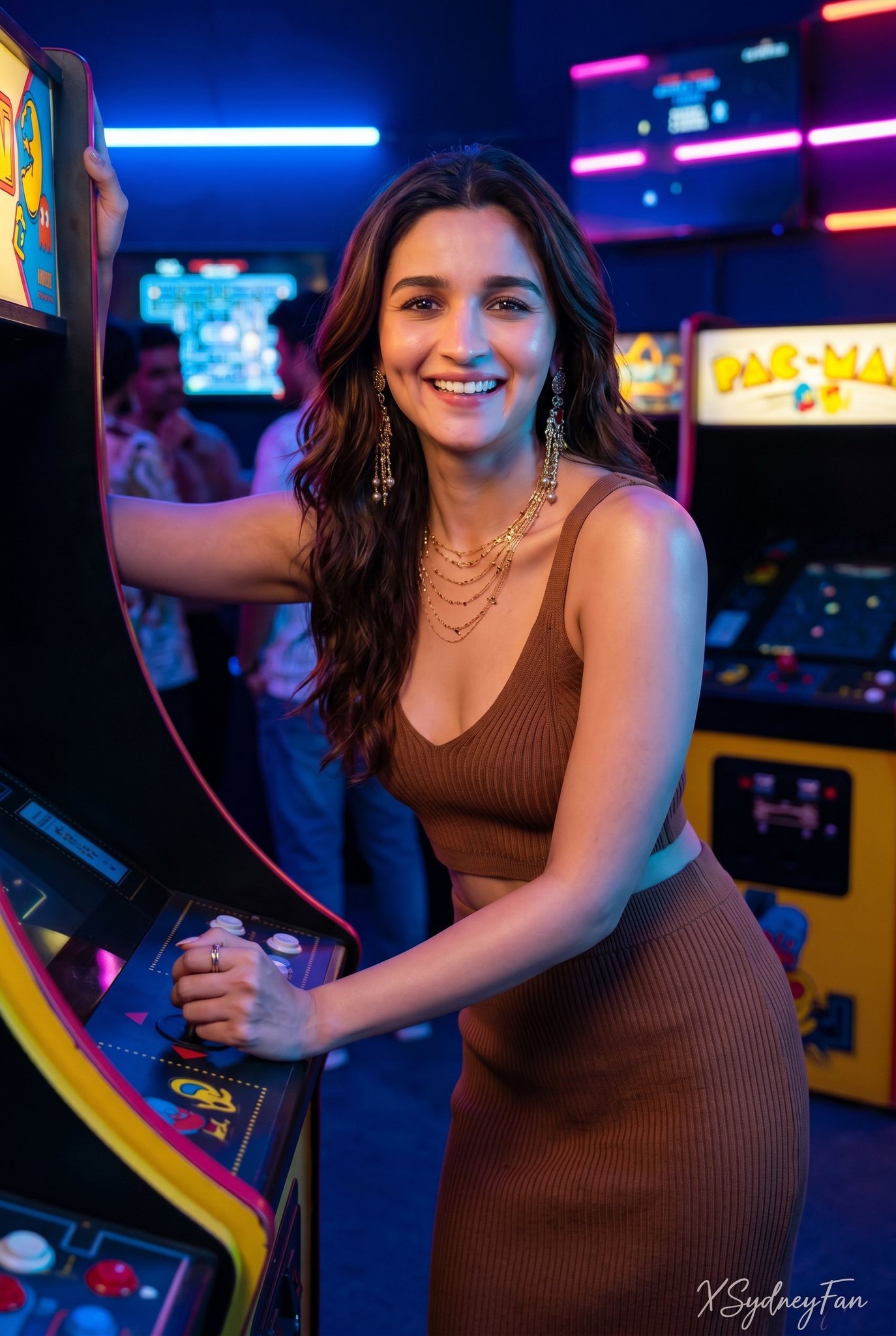 Woman in brown ribbed bikini top and bottoms poses by arcade machine, large gold earrings and necklace.