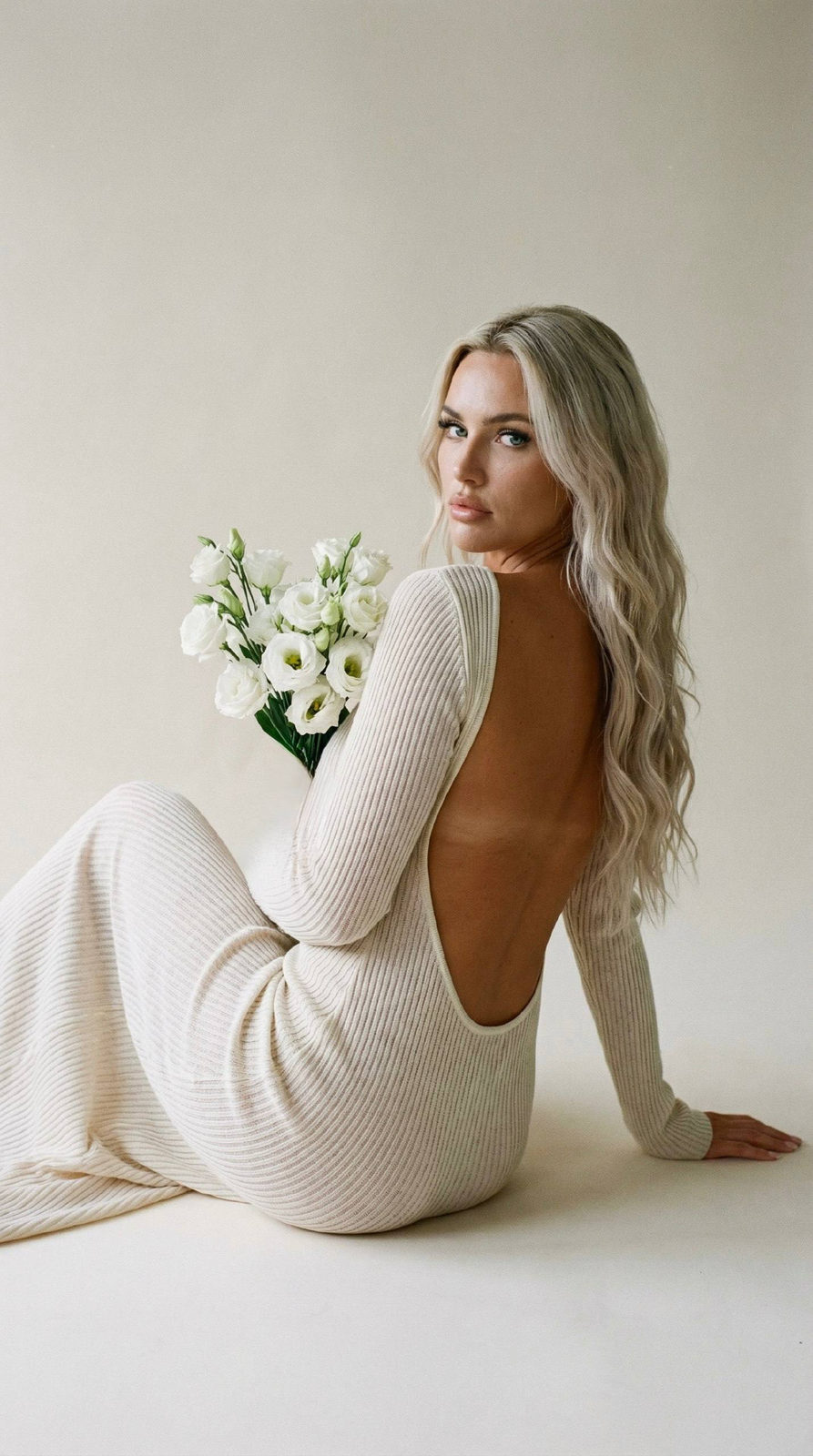 A female portrait featuring film grain texture, with a warm ivory dress, holding white eustoma flowers, softly lit against a beige background.