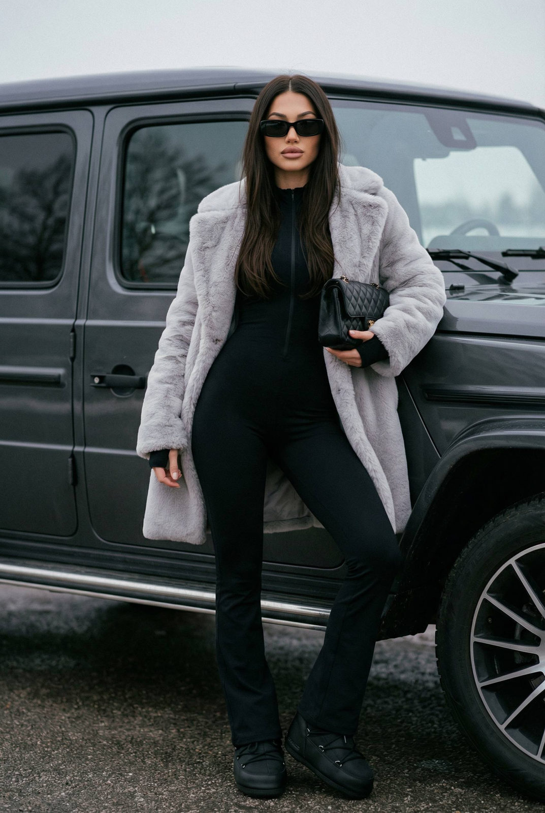 A confident woman in a fitted jumpsuit and faux-fur coat leaning against an SUV, wearing sunglasses and a Chanel-style bag.